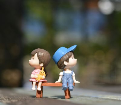 pexels-photo-1767434-1767434 Adorable figurines of a boy and girl sit on a bench, bathed in summer sunlight.